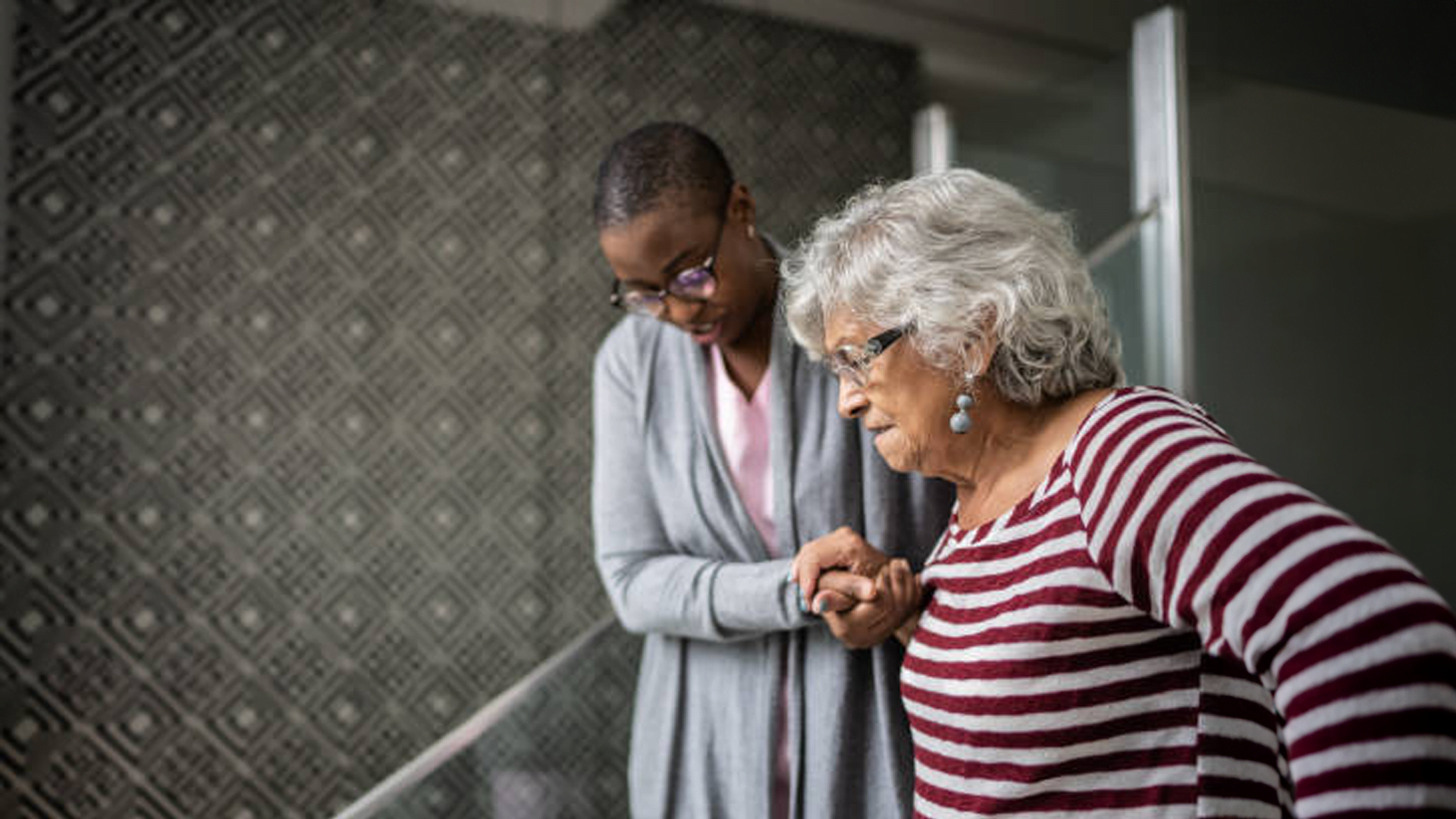 An older woman with mecfs is looking at her phone with a caregiver.