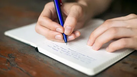 A person with ME/CFS writing in a notebook with a pen.