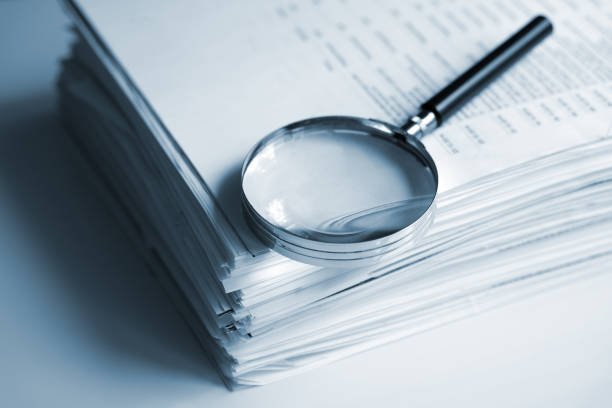 A magnifying glass inspecting a stack of mecfs documents.