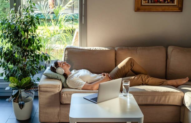 A man with mecfs is laying on a couch with a laptop on his lap.