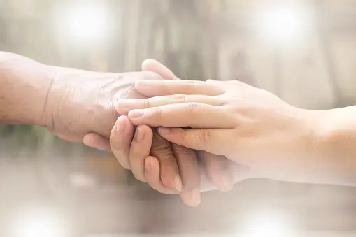 Two individuals with mecfs holding hands, amidst a blurry backdrop.