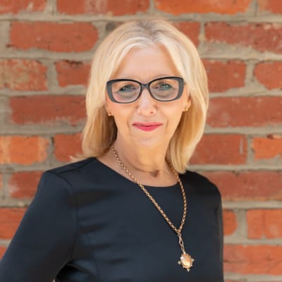A woman in glasses standing in front of a brick wall represents resilience amidst the challenges of living with mecfs.