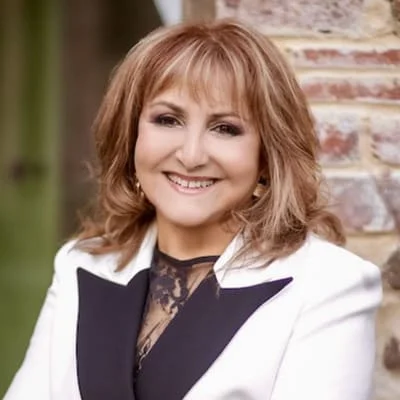 A woman with mecfs wearing a white blazer and black jacket smiles.