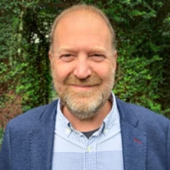 A man with mecfs smiling in front of bushes.