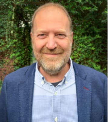 A man with a beard standing in front of bushes, representing mecfs awareness.