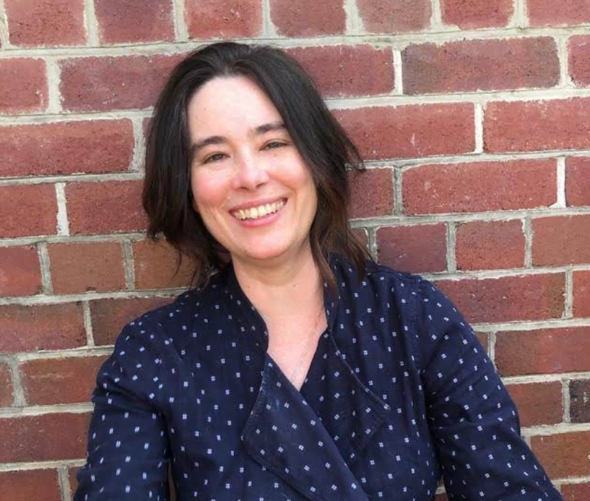 An upbeat woman grinning in front of a brick wall.
