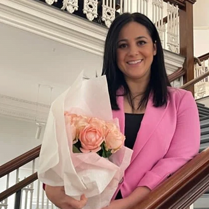 A woman with ME/CFS in a pink jacket holding a bouquet of flowers.