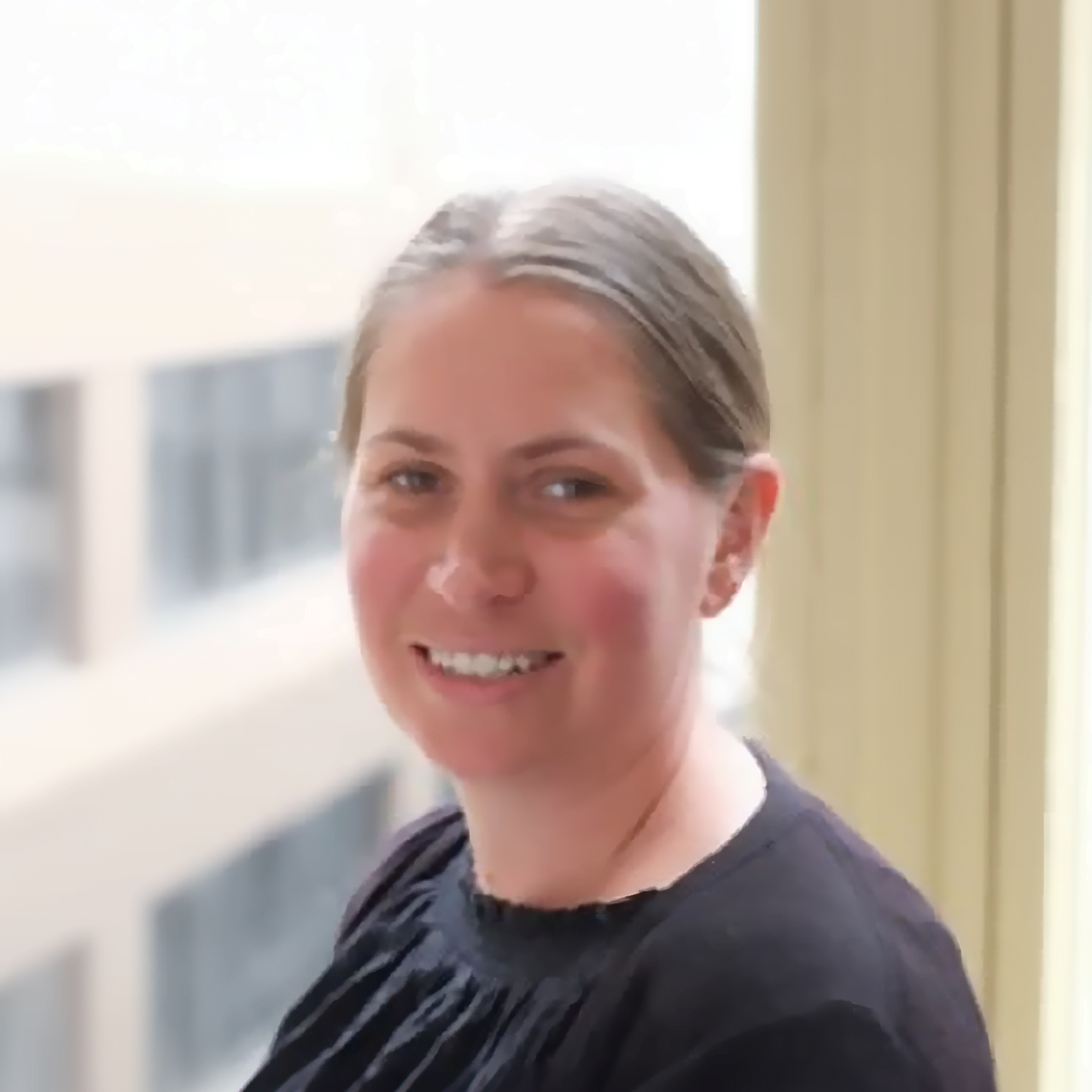 A woman smiling in front of a window, overcoming mecfs.