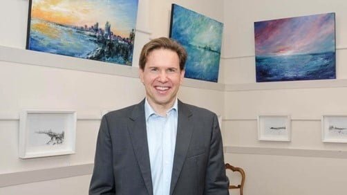 A suit-clad man observing paintings.