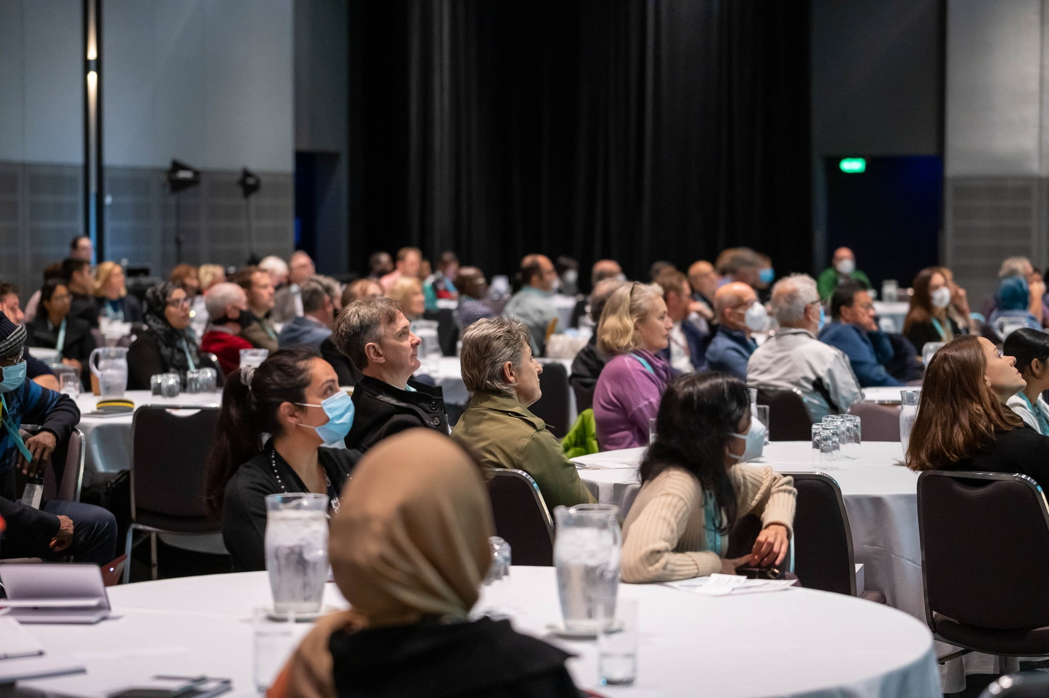 A crowd of people sitting at tables in a conference room discussing the impact of ME/CFS.