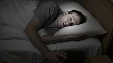 A man with mecfs is sleeping in bed with an alarm clock.