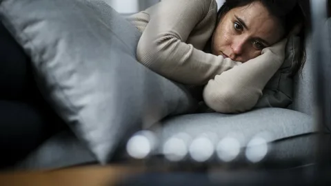 A woman with mecfs laying on a couch with her head resting on her hand.